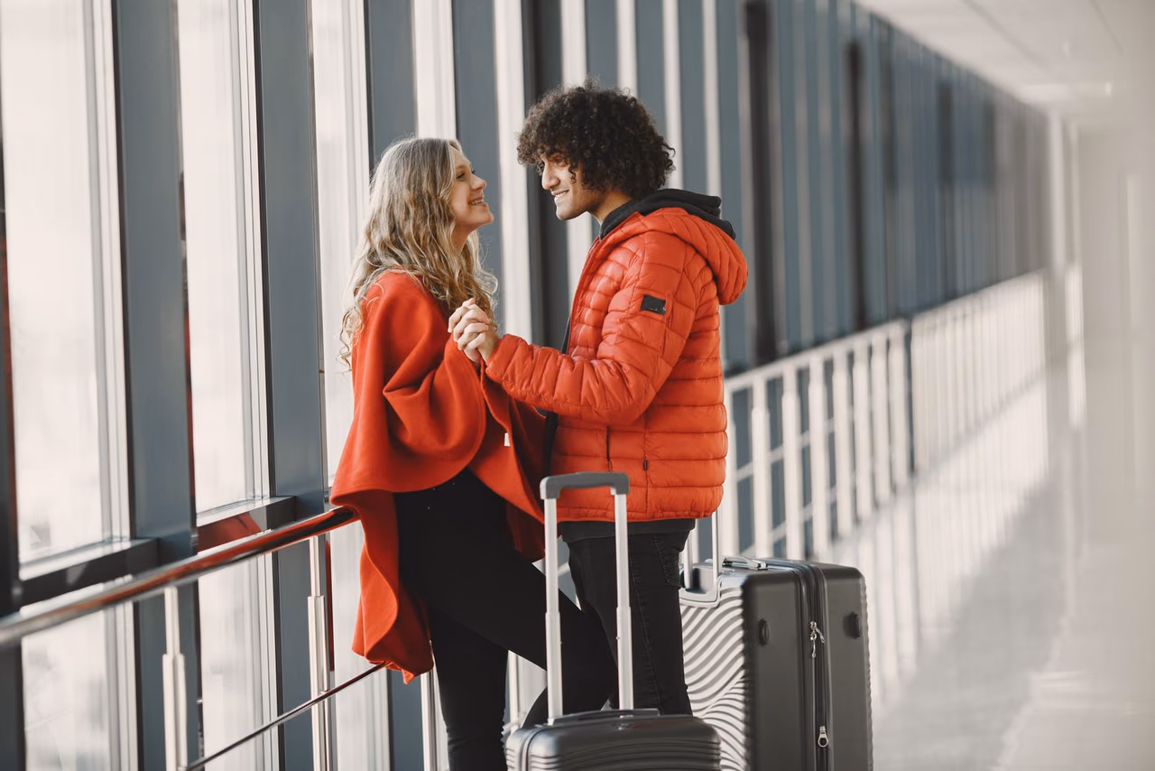 A couple holding hands and pulling suitcases through an airport terminal