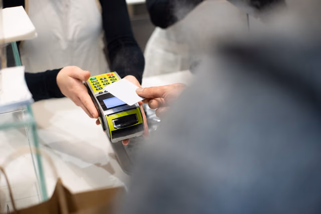 A customer holding a card to a payment terminal at the counter of a modern retail store