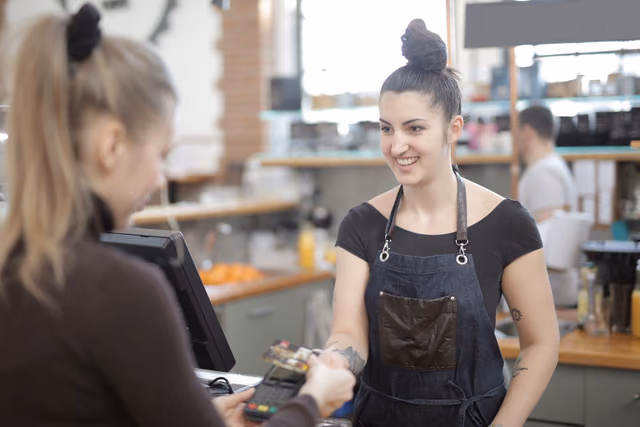 Customer paying with a credit card at a cafe counter while a barista in an apron holds the card reader
