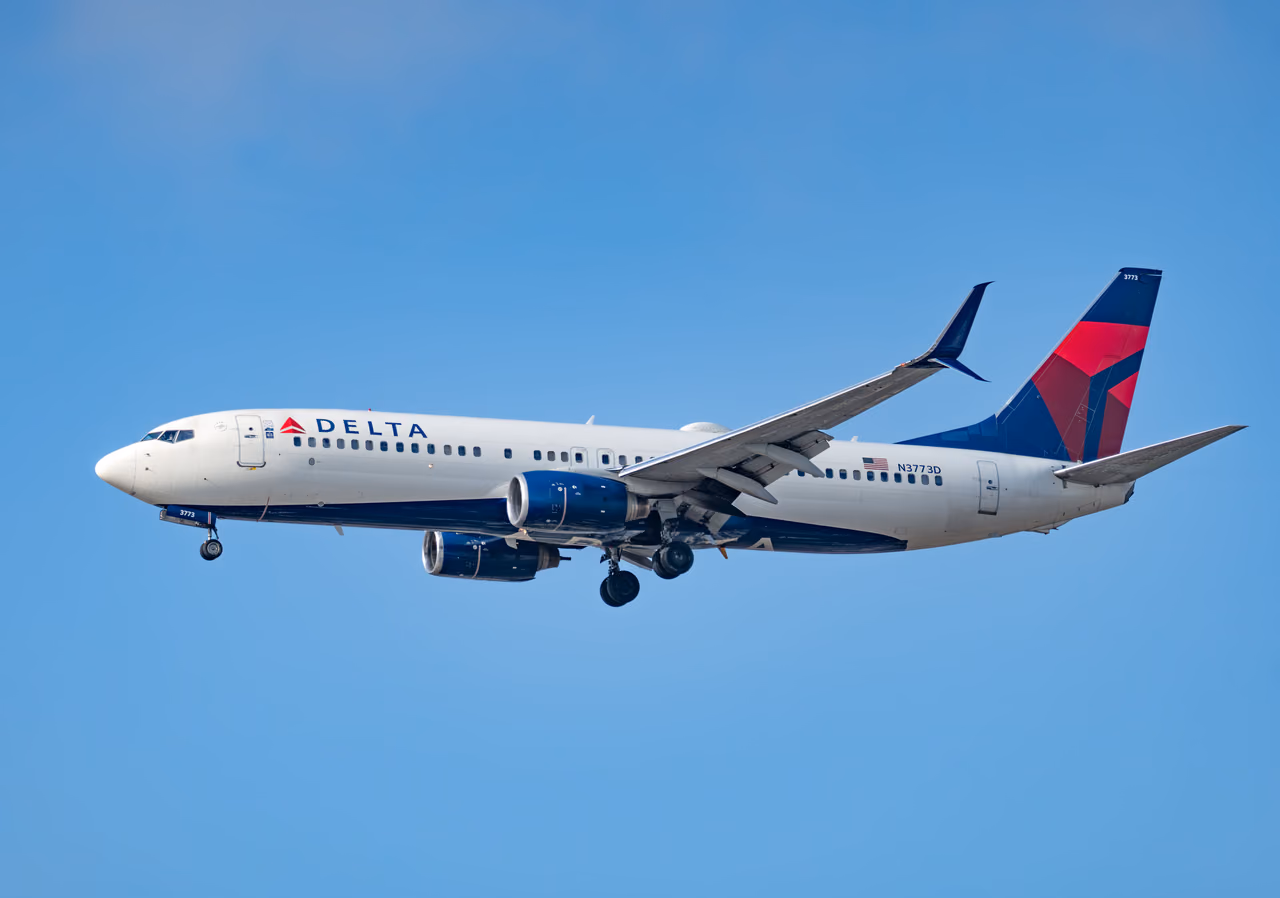 A Delta Air Lines Boeing 737 in flight with landing gear down against a clear blue sky
