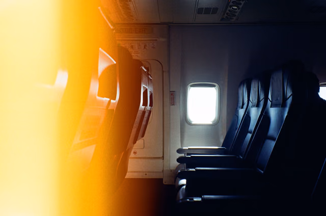 Empty black airplane seats beside a window with warm light falling across the cabin