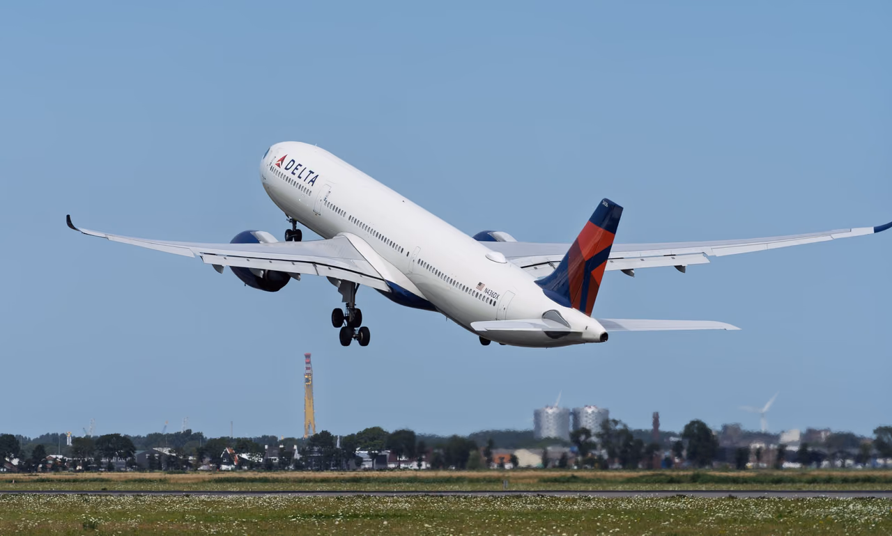 A Delta Air Lines twin-engine jet climbing away from a runway with its landing gear still down under a clear blue sky