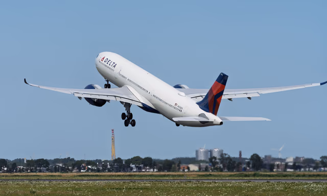 A Delta Air Lines twin-engine jet climbing away from a runway with its landing gear still down under a clear blue sky