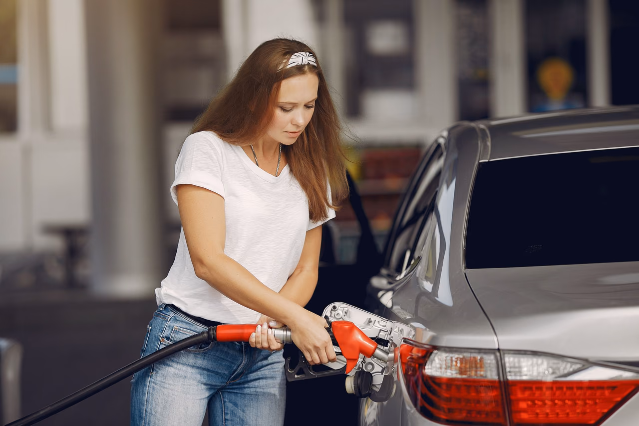 A driver holding a fuel nozzle while filling a car at a gas station