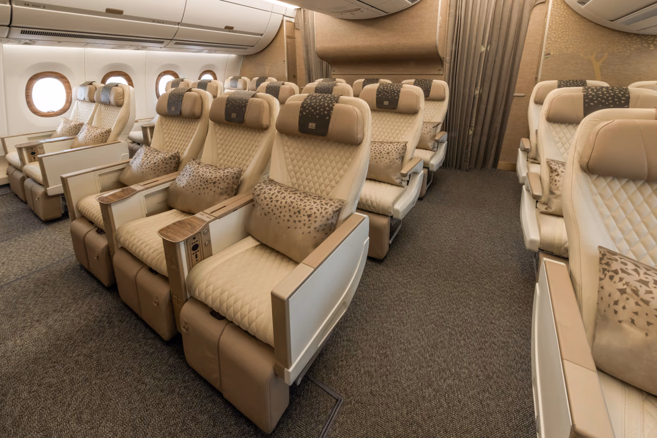 Cream Premium Economy seats with patterned cushions and wood-trimmed armrests in an Emirates A350 cabin, arranged in rows beside oval windows