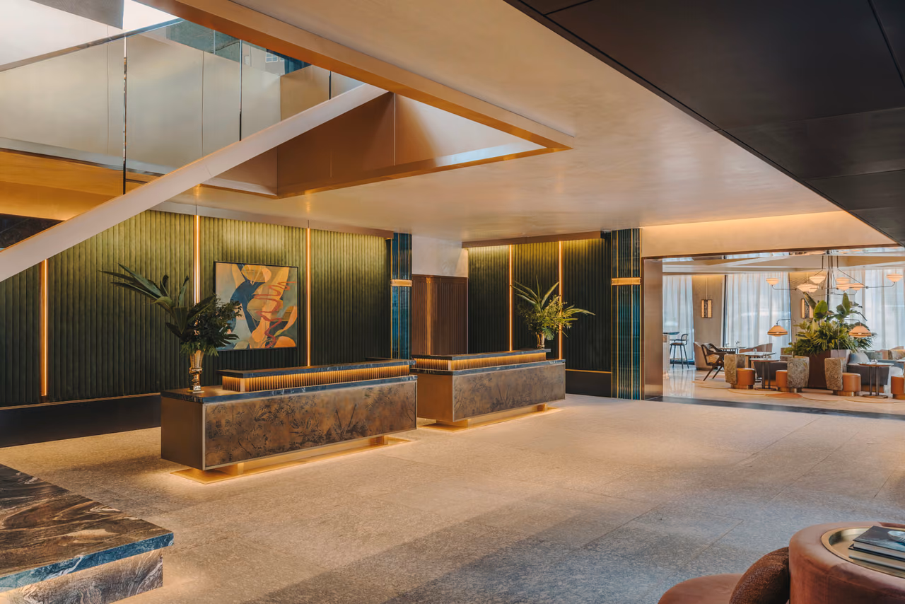 The lobby of Fairmont New Orleans with two stone reception desks against a green fluted wall and a lounge with seating beyond