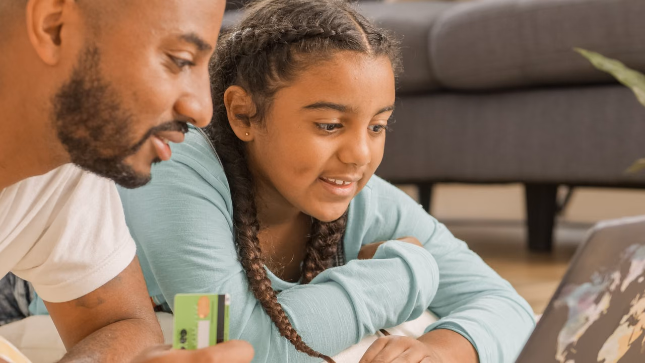 A father and daughter using a laptop and credit card together at home