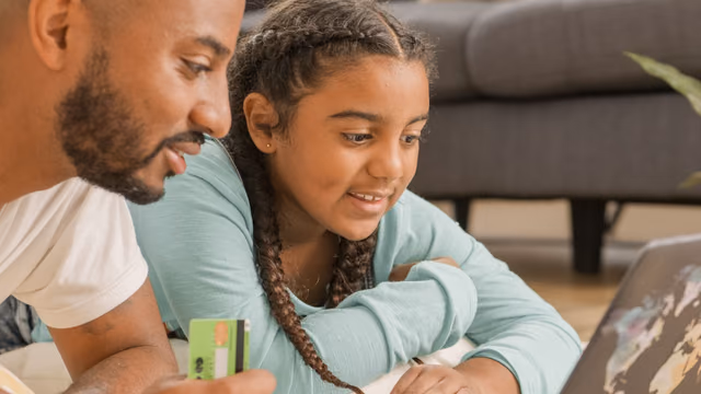 A father and daughter using a laptop and credit card together at home