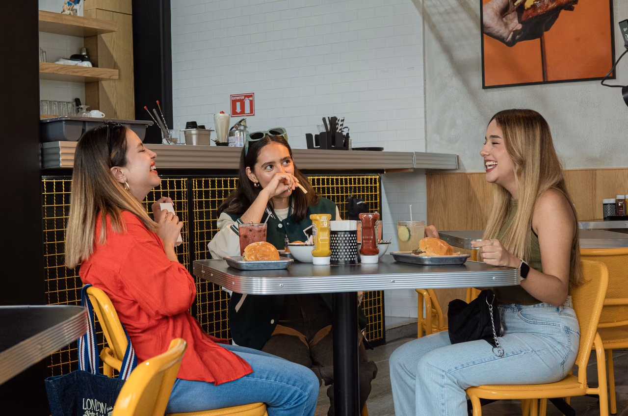 Three friends laughing over burgers at a table in a modern restaurant