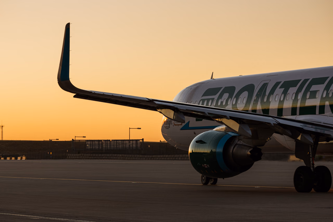 A Frontier Airlines Airbus jet on the tarmac at sunset, its green-lettered fuselage and swept wing against an orange sky