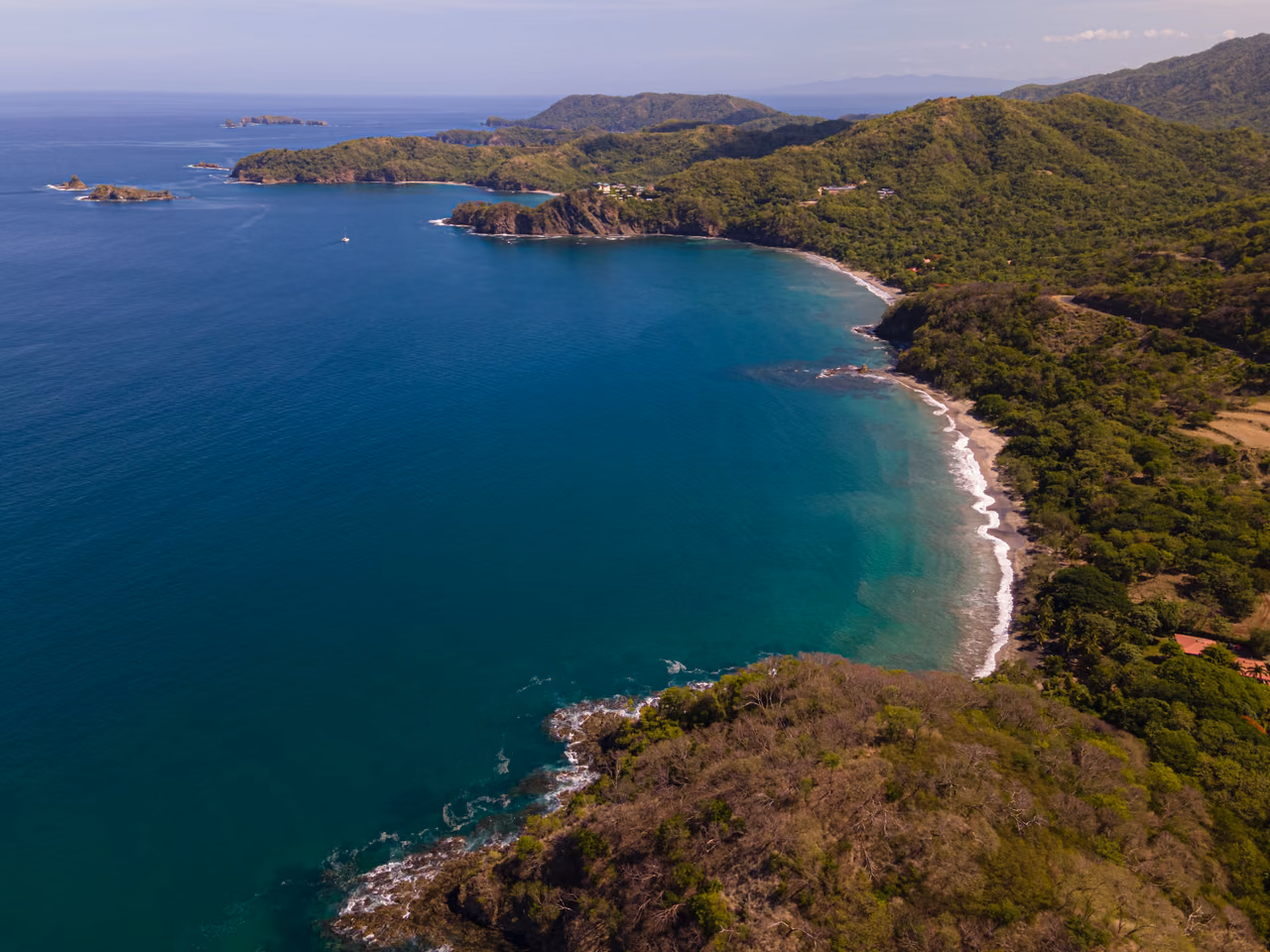 Aerial view of a curved bay on Costa Rica's Guanacaste coast, with turquoise water and green forested hills
