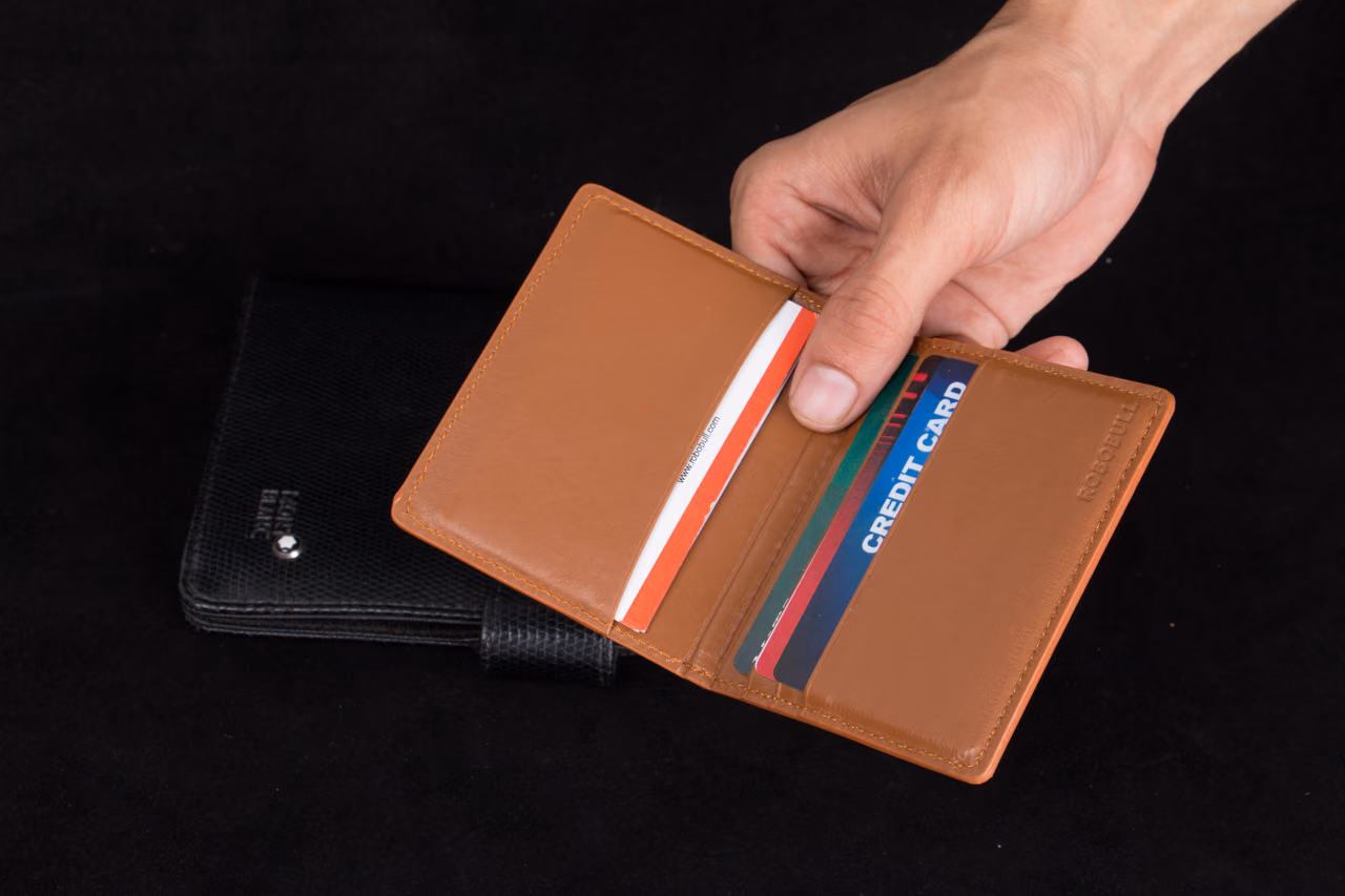 A hand holding an open brown leather wallet filled with credit cards