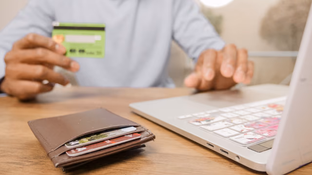 Hands holding a bank card in front of an open laptop