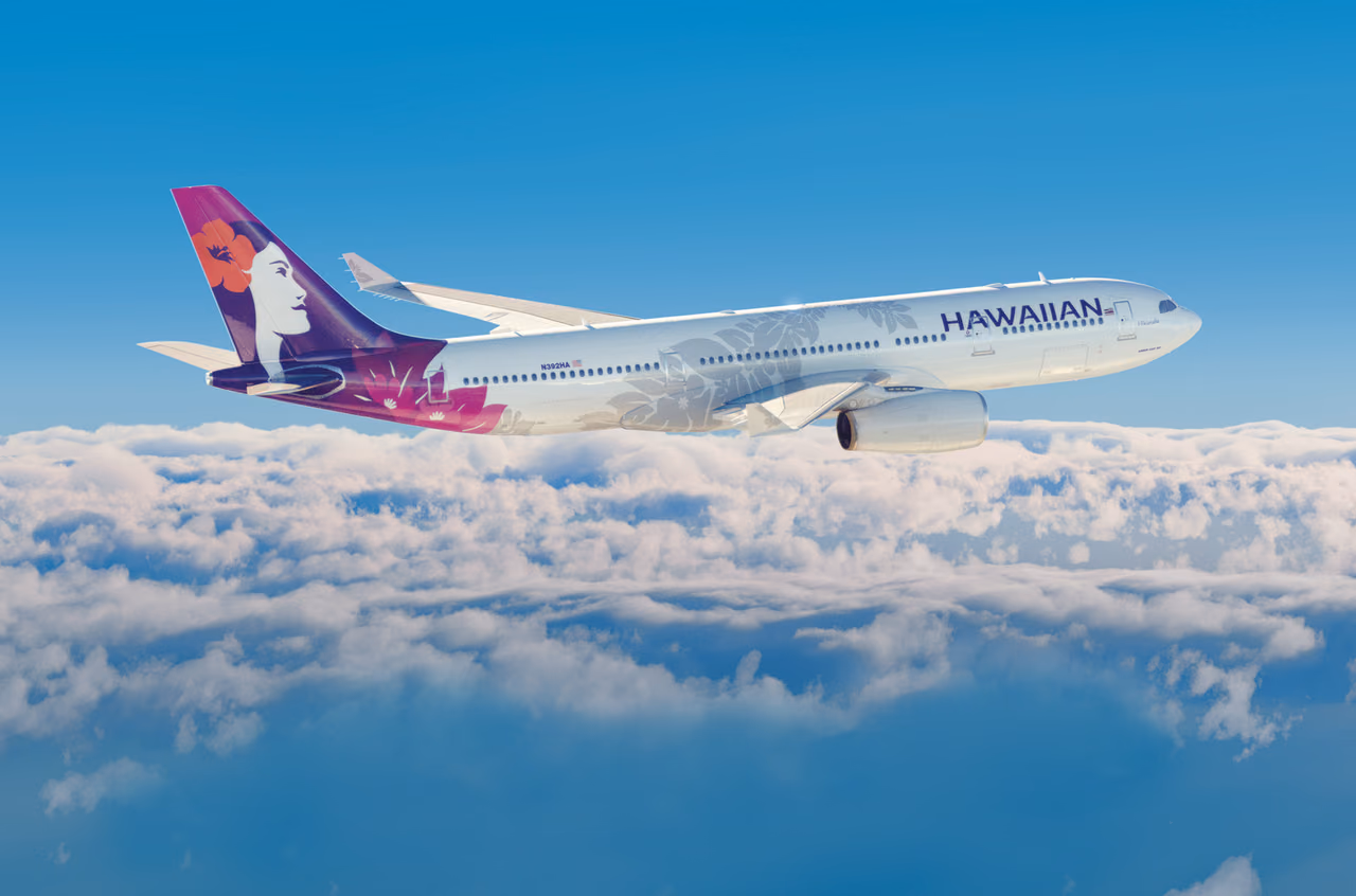 Hawaiian Airlines Airbus A330 with a purple hibiscus tail flying above a layer of white clouds under a clear blue sky