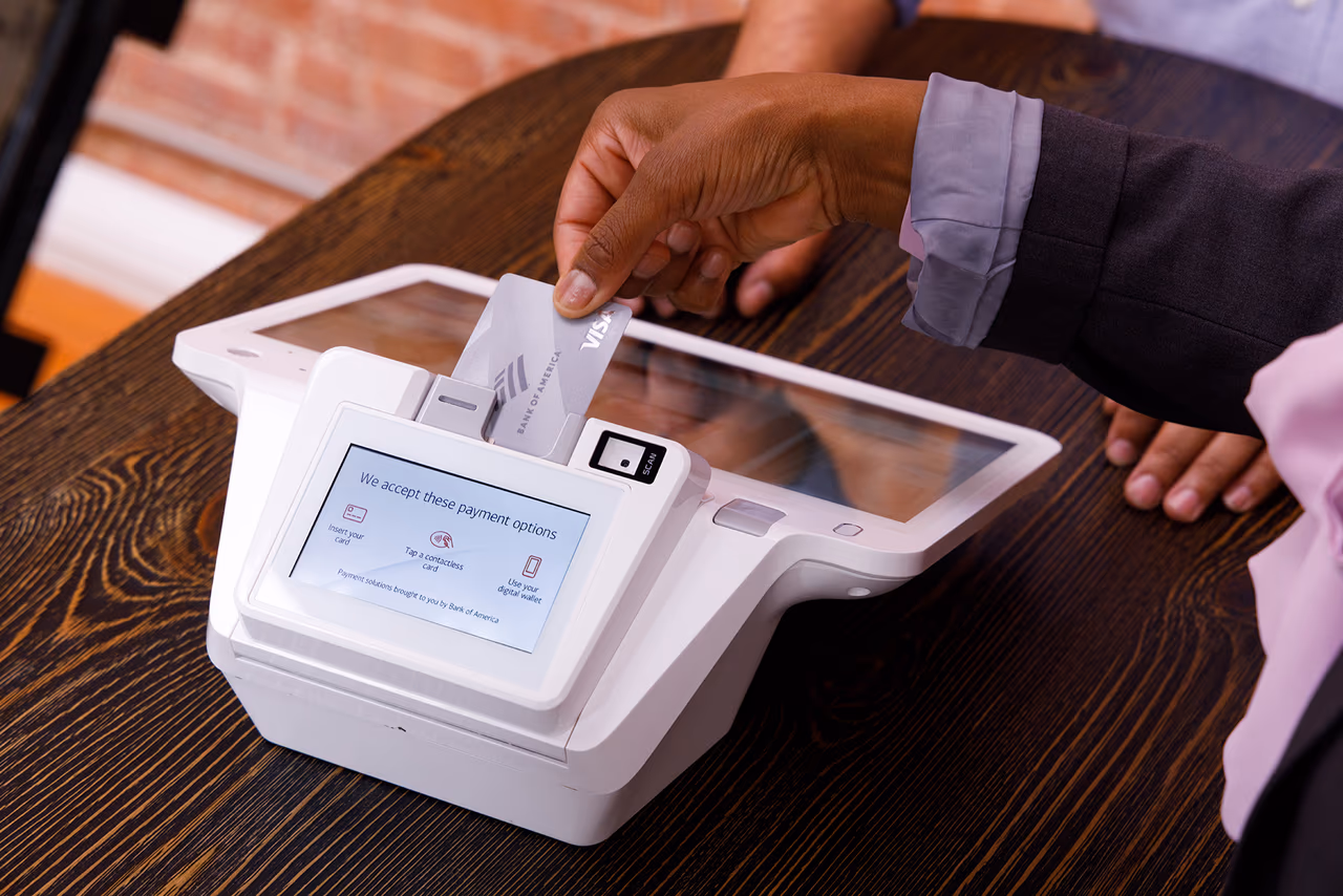 A close-up of a hand inserting a credit card into a countertop card reader at a shop counter