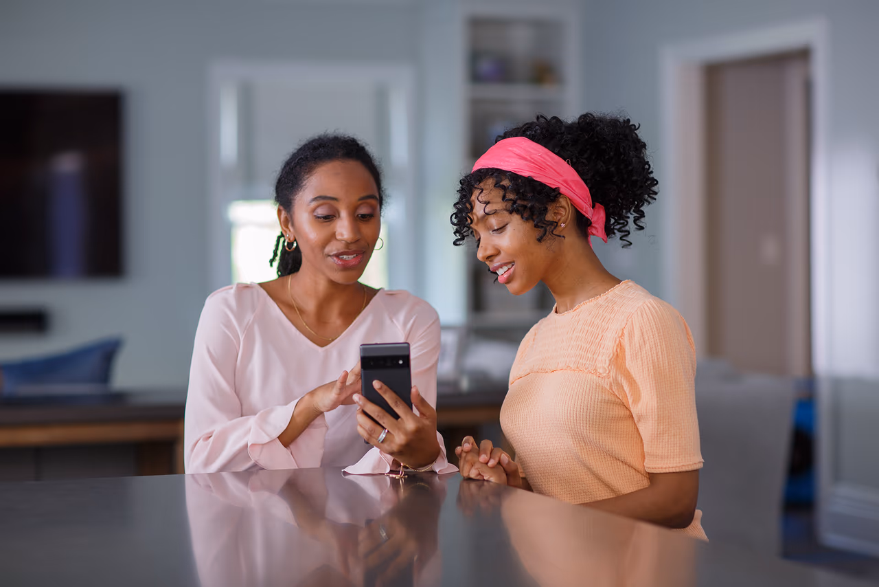 A parent and child sitting together in a kitchen looking at a smartphone screen