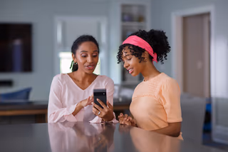 A parent and child sitting together in a kitchen looking at a smartphone screen