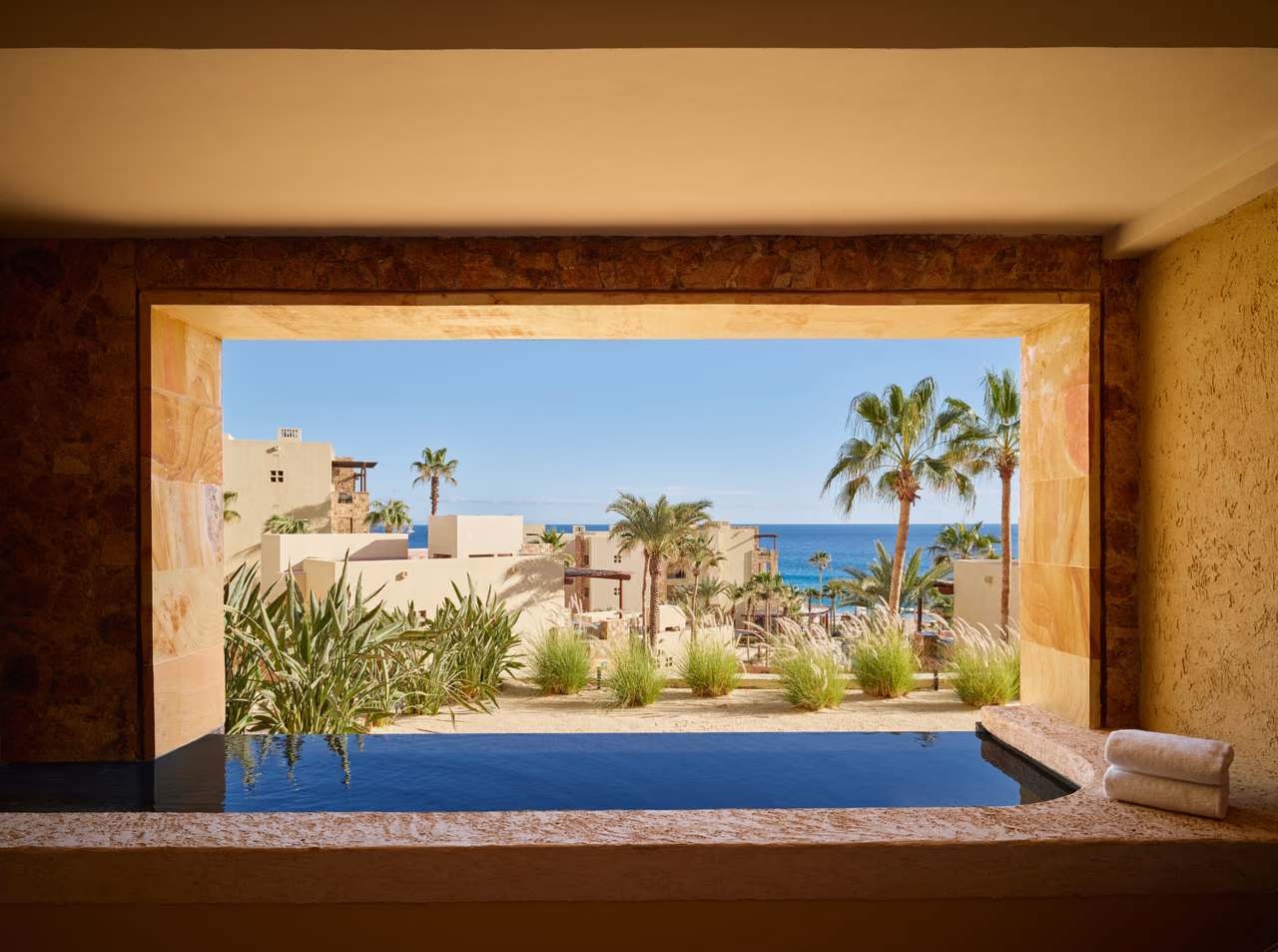 A private plunge pool framed by a stone window, looking out over palm trees and the ocean at Waldorf Astoria Los Cabos Pedregal.