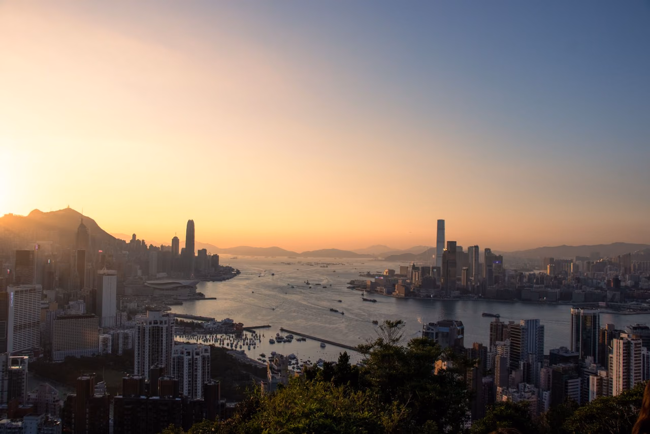 Hong Kong's skyline and Victoria Harbour at sunset, seen from a hillside with boats on the water