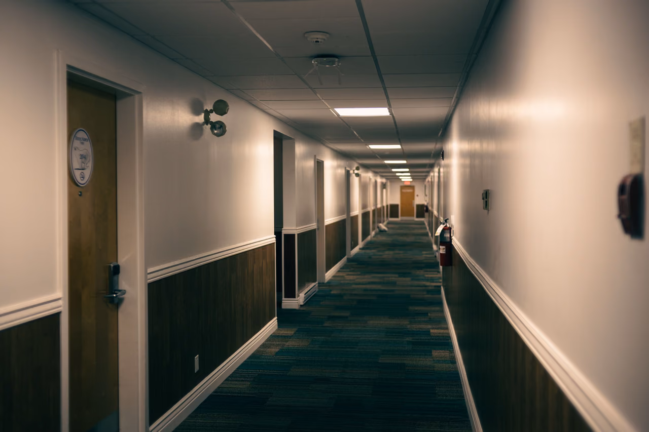 A long hotel hallway with patterned blue carpet, wood-paneled lower walls and guest room doors on both sides