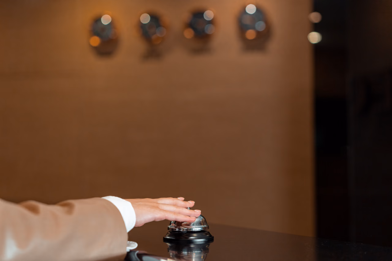 A hand pressing the silver call bell on a hotel reception desk
