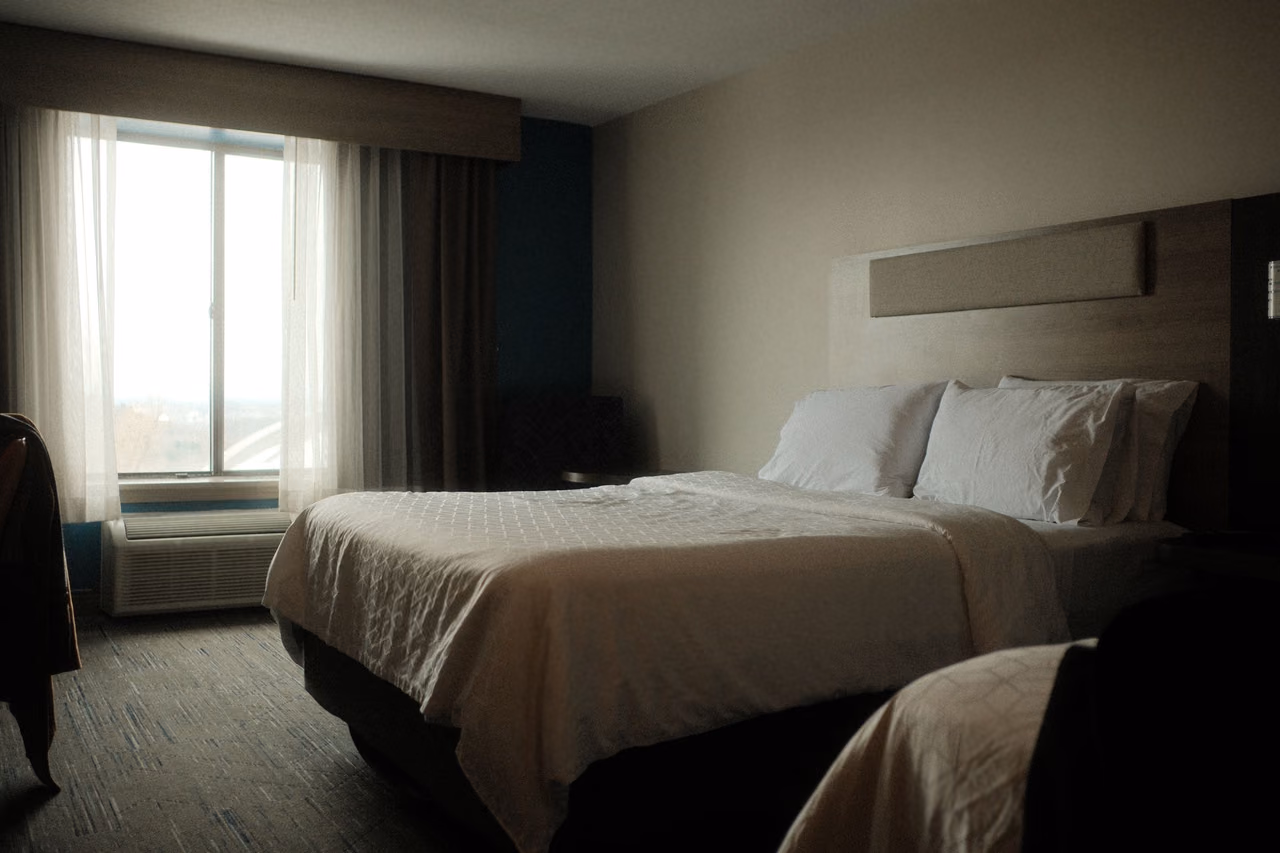 A hotel room with a made bed and soft morning light coming through a tall window