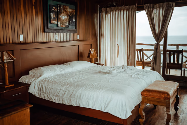 A hotel room with white bed linen and an ocean view through the window