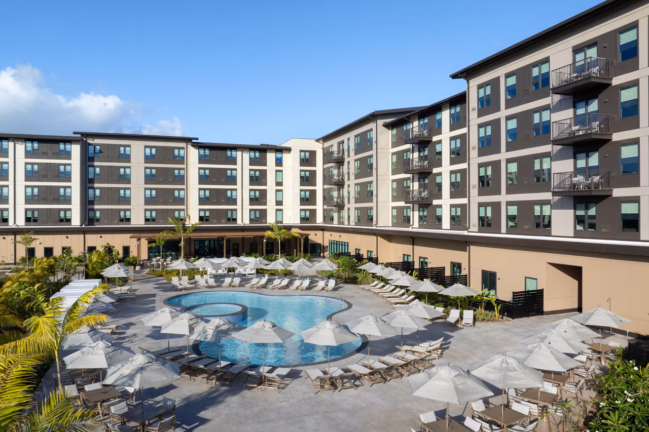 Outdoor pool ringed by white umbrellas and lounge chairs in the courtyard of Hyatt Place at Ho'opili in Ewa Beach, Oahu