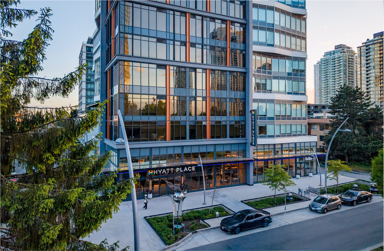 Glass hotel tower with a Hyatt Place sign over the street-level entrance, trees in front and cars parked at the curb