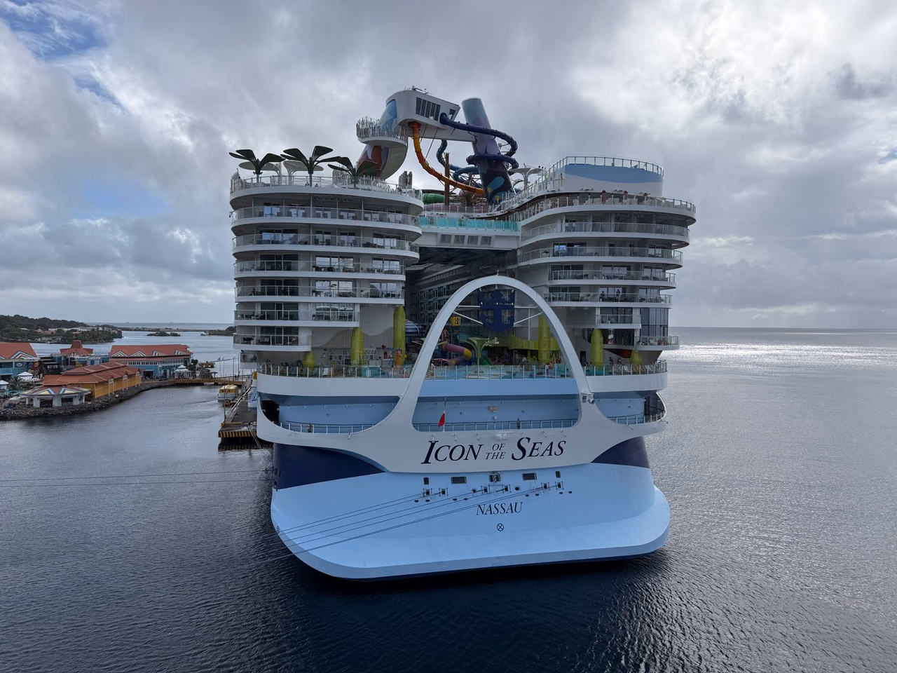 Stern view of Royal Caribbean's Icon of the Seas docked at a harbor, with stacked balcony decks and waterslides above the aft