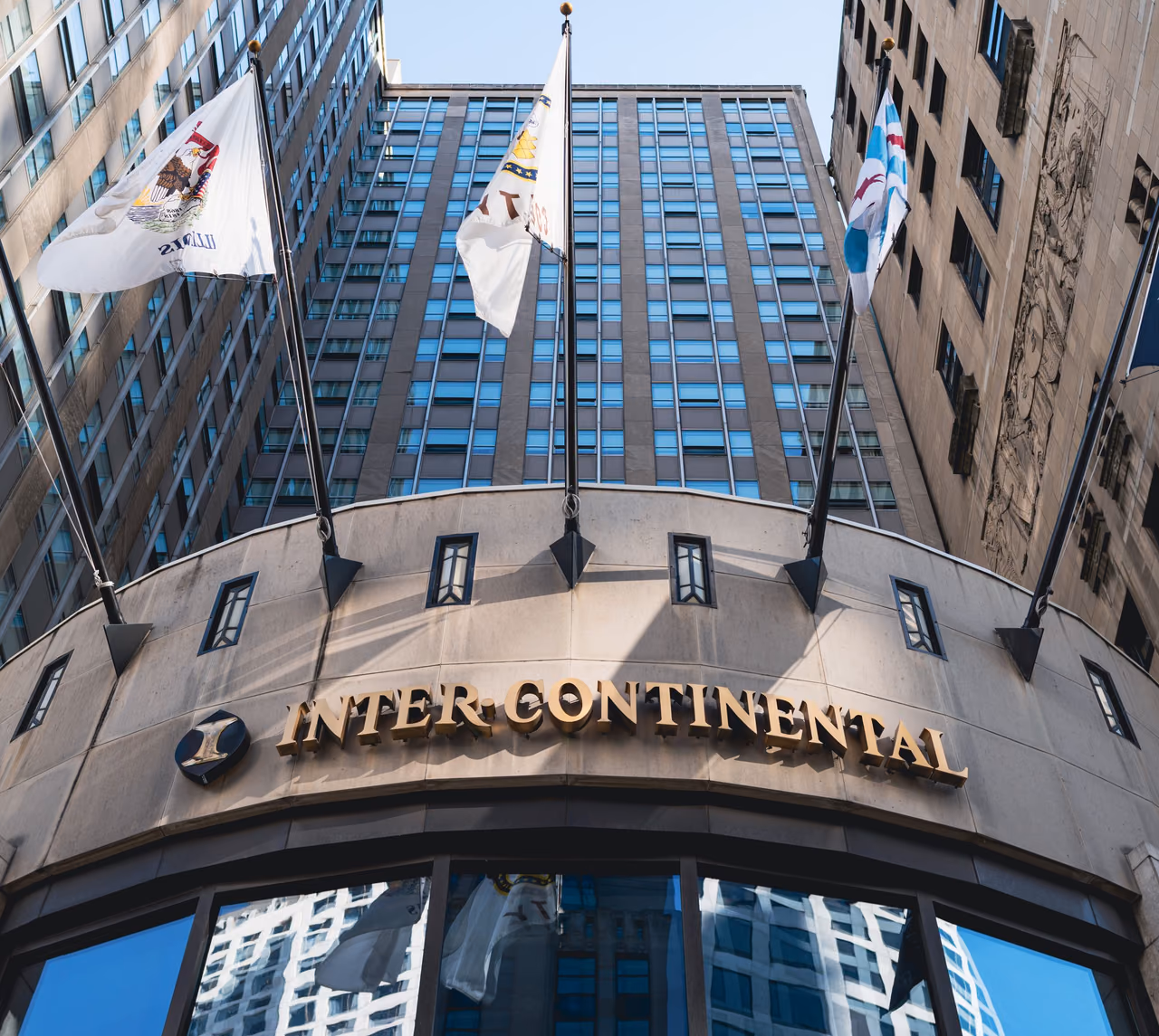 The gold Inter-Continental sign and flags above the curved entrance of the InterContinental Chicago, seen from below