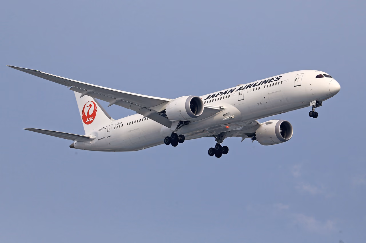 A Japan Airlines Boeing 787 with the red crane logo on its tail, landing gear down against a pale sky