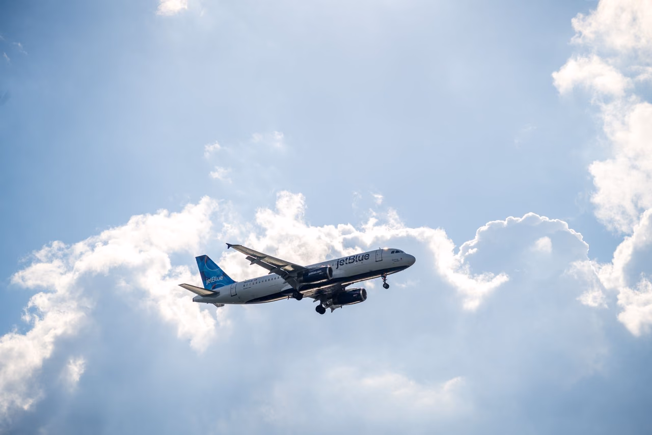 JetBlue Airbus A320 with its landing gear down flying past large white clouds in a blue sky