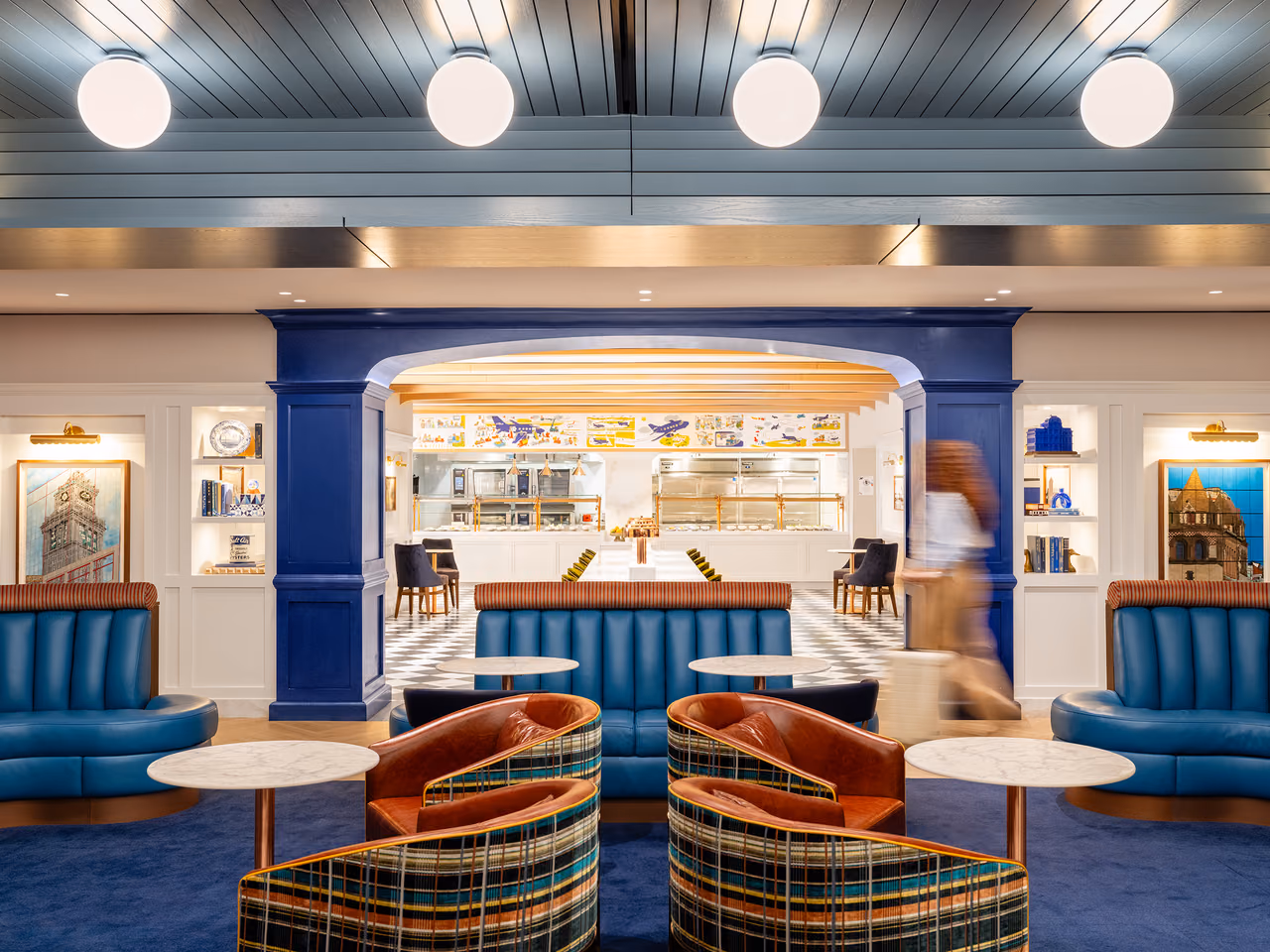Blue booths and plaid swivel chairs in JetBlue's BlueHouse lounge at Boston Logan, with the food counter visible through a blue archway