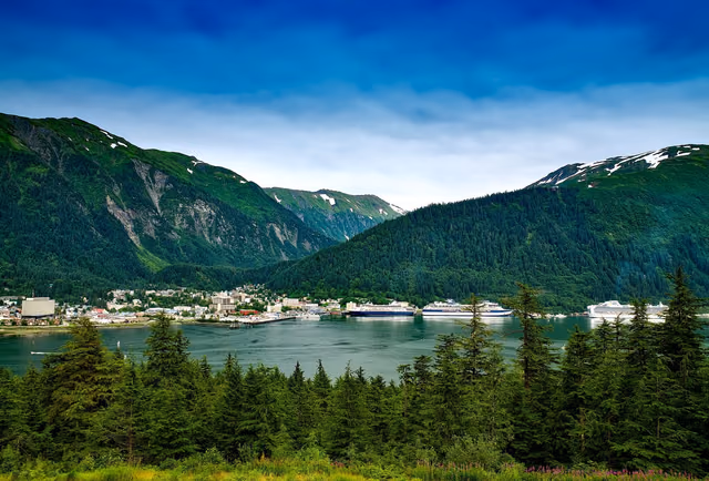 Downtown Juneau, Alaska on the waterfront with cruise ships at the docks and forested mountains rising behind the city