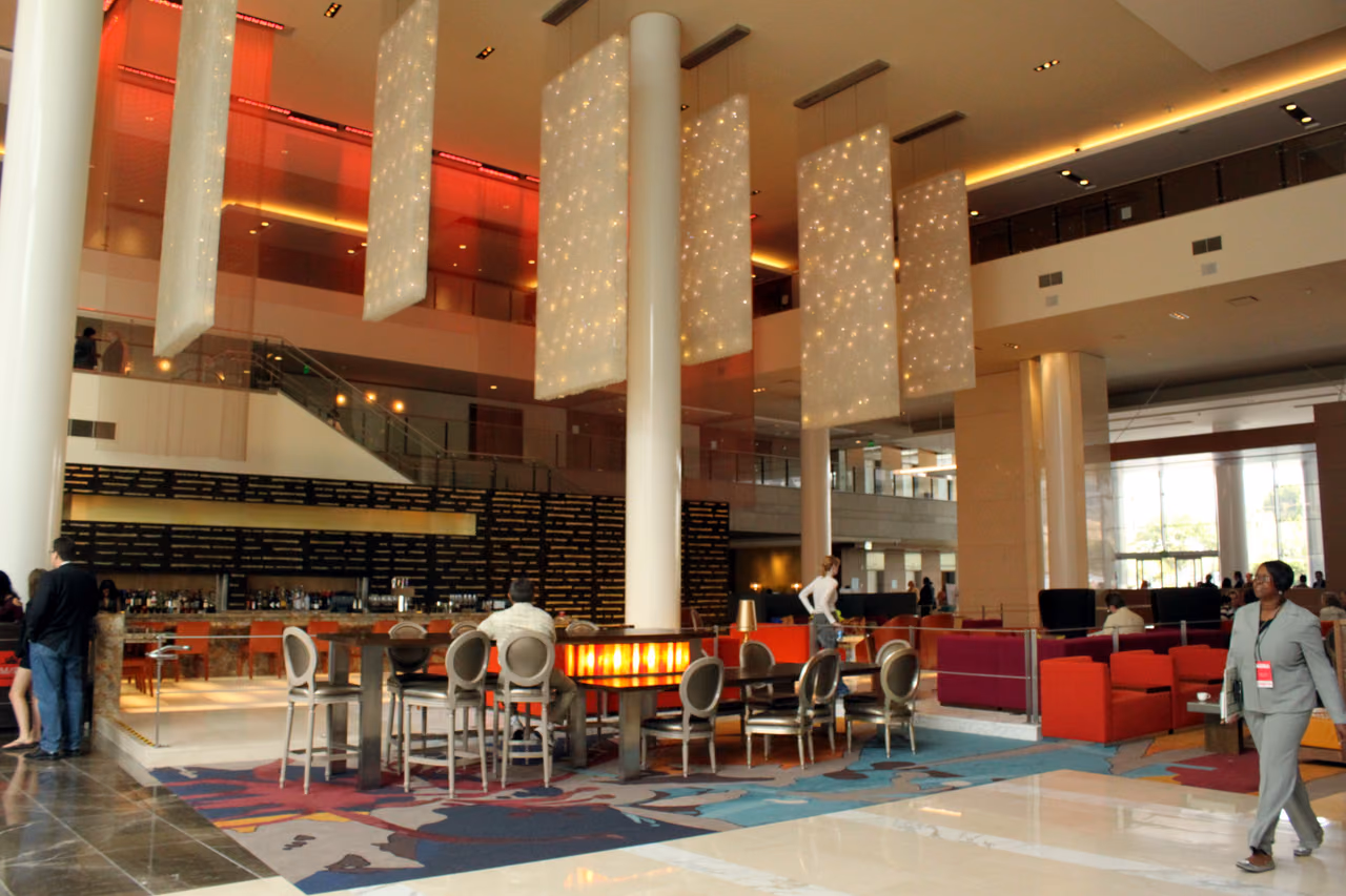 The lobby of the JW Marriott Los Angeles, with tall white columns, hanging light panels, a bar and red lounge seating