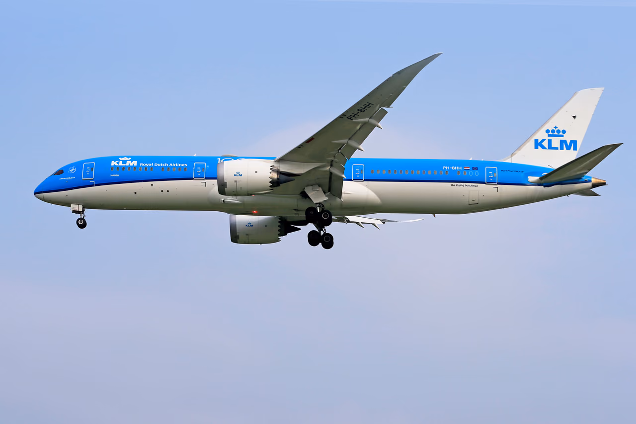 KLM Boeing 787 Dreamliner in blue and white livery flying with landing gear down against a pale sky
