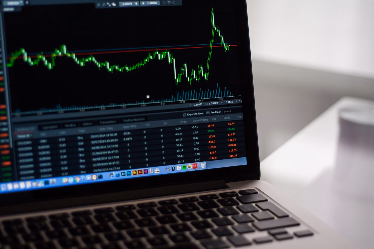 Laptop screen showing a green line chart of price movements above a table of trading data