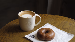 Latte in a white cup beside a chocolate bagel on a wooden cafe table