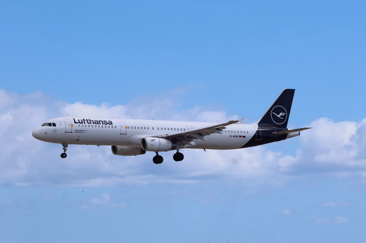 Lufthansa Airbus A321 in the white and dark blue livery flying with landing gear down under a blue sky with clouds