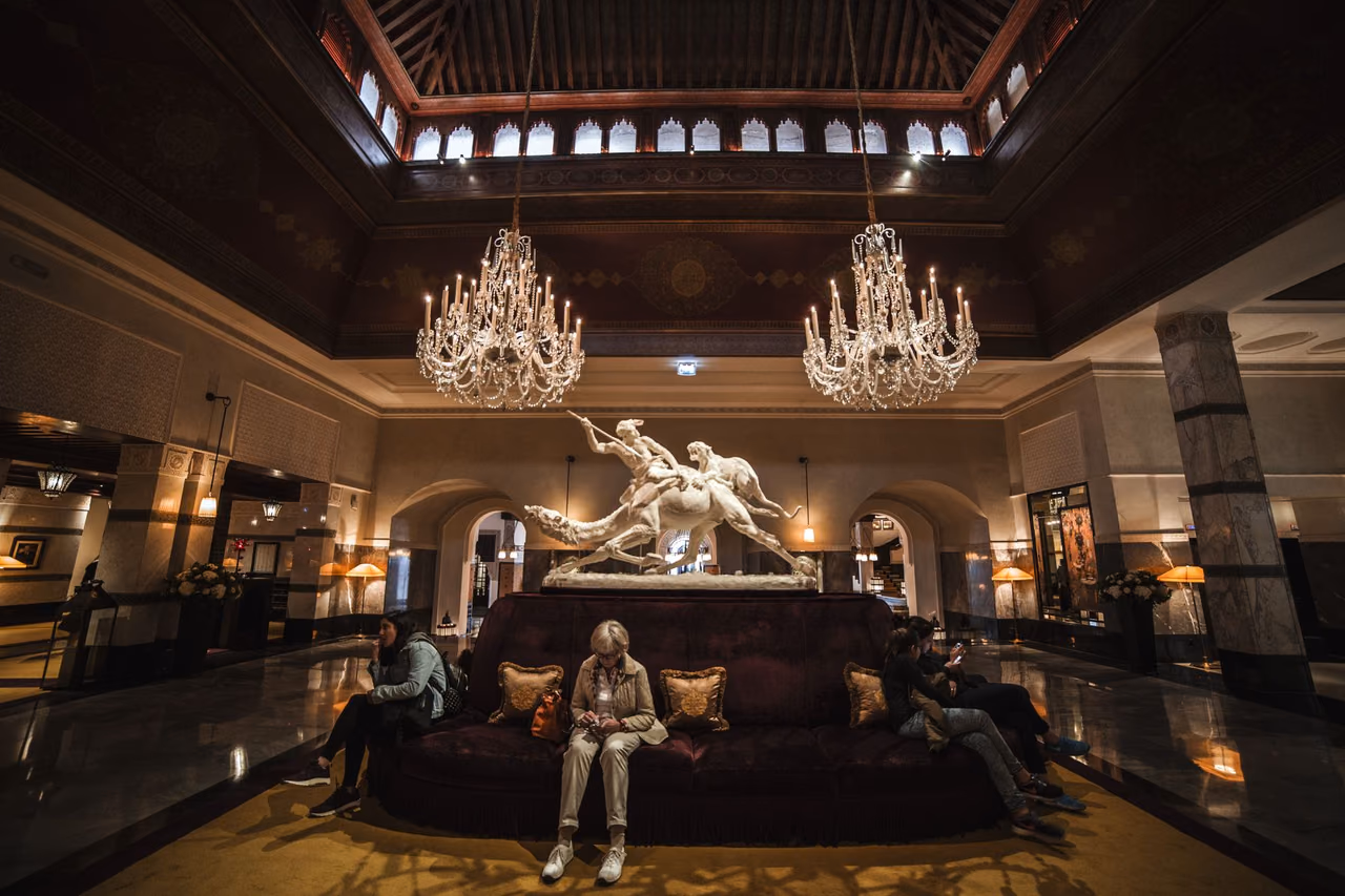 A spacious luxury hotel lobby with sofas, crystal chandeliers and a marble statue
