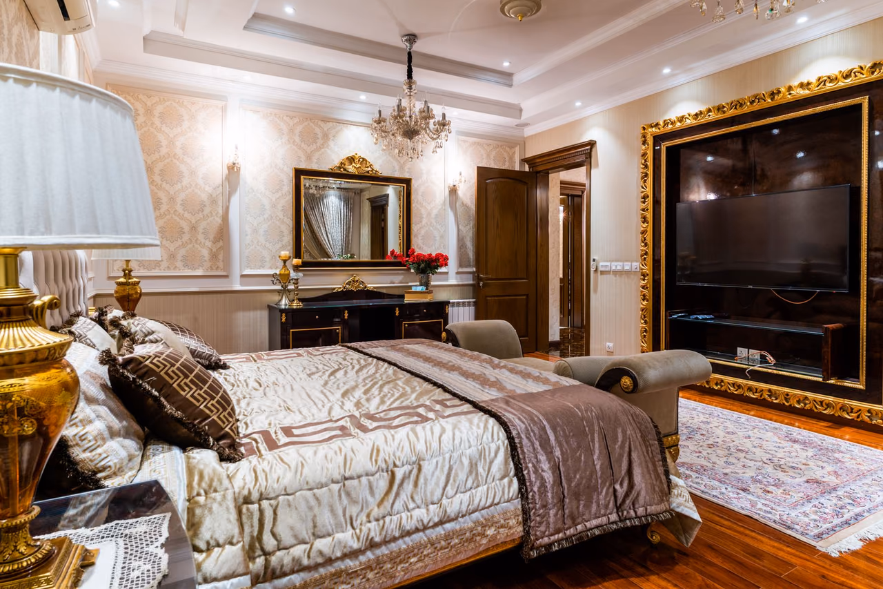 An elegant hotel bedroom with a chandelier, a large mirror and gold accents