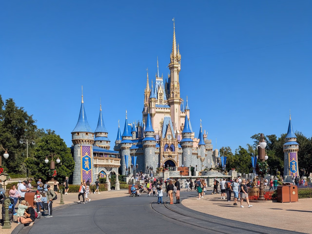 Cinderella Castle at Magic Kingdom under a clear blue sky, with visitors walking along the path in front
