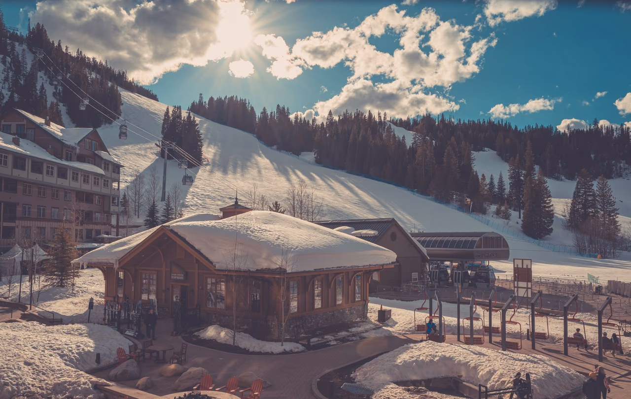 Snow-covered wooden lodge at the base of a ski slope with a ski lift and pine forest behind it