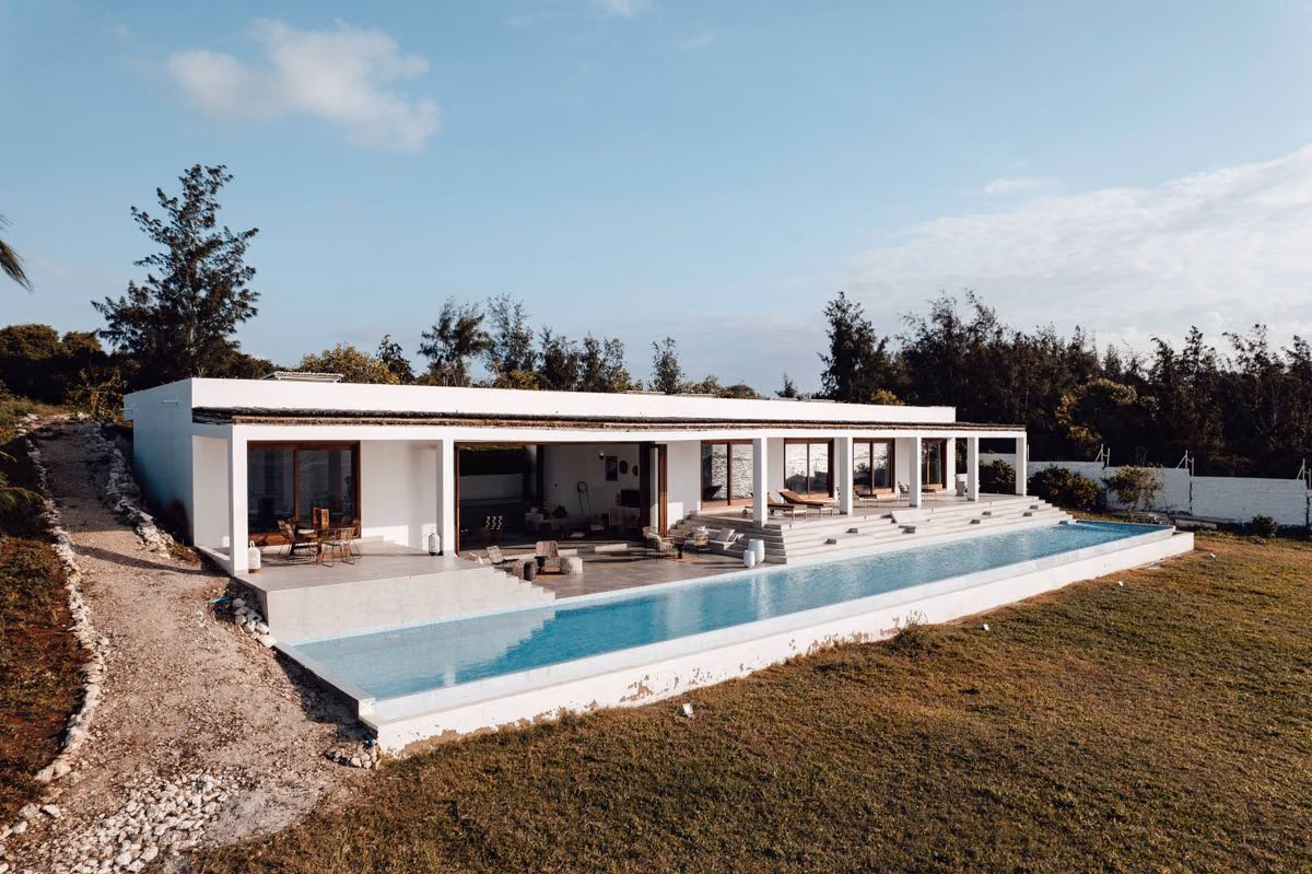 A white modern villa with an infinity pool and green landscaping under a blue sky