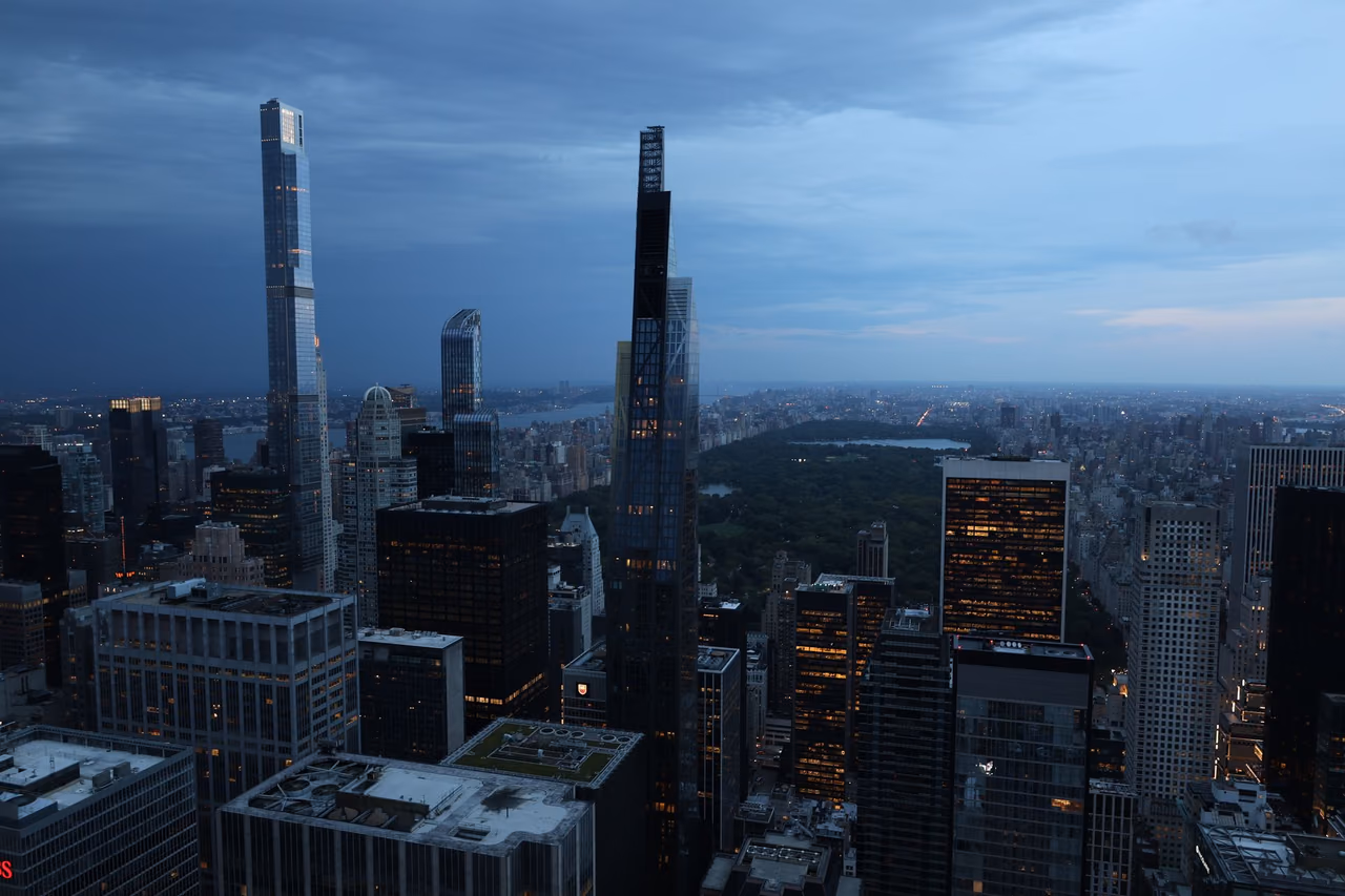 Midtown Manhattan skyscrapers at dusk under a cloudy blue sky, with Central Park and the city stretching to the horizon