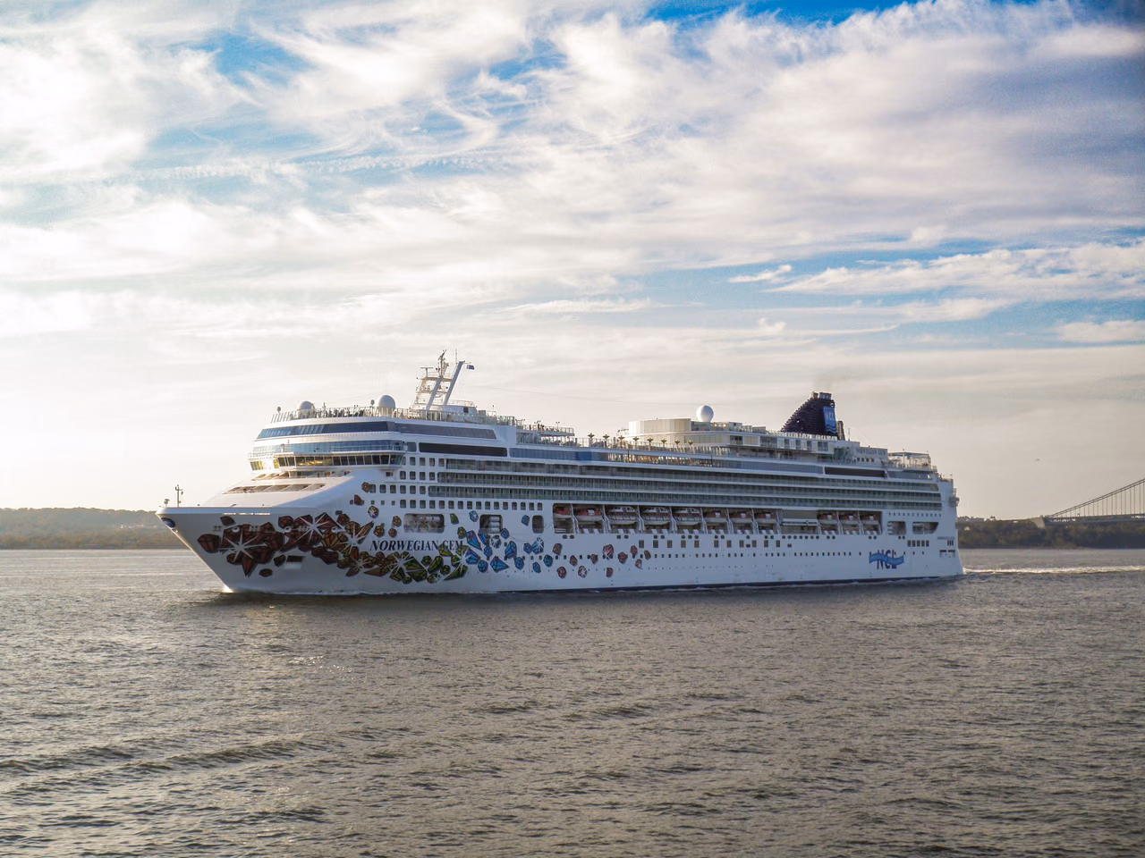 The cruise ship Norwegian Gem, with its colorful hull art, sailing on calm water under a partly cloudy sky