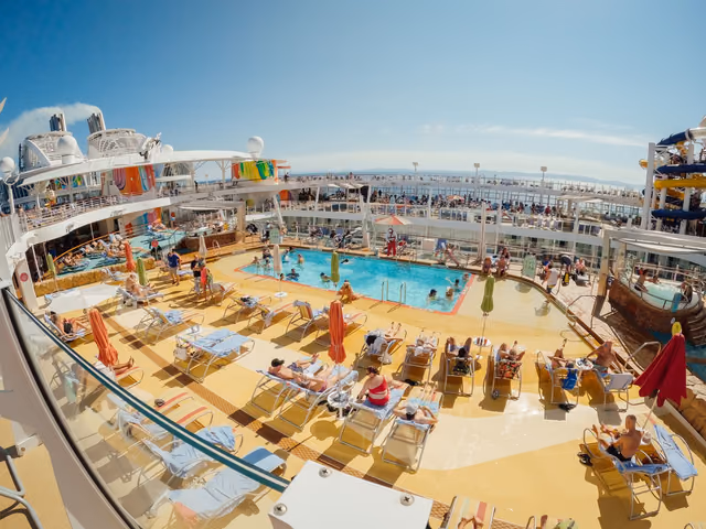 Passengers relax on loungers around the main pool on the pool deck of Royal Caribbean's Oasis of the Seas, with waterslides on the right and the open sea beyond