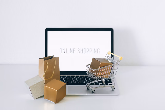 A laptop open to an online store beside cardboard boxes and a shopping cart