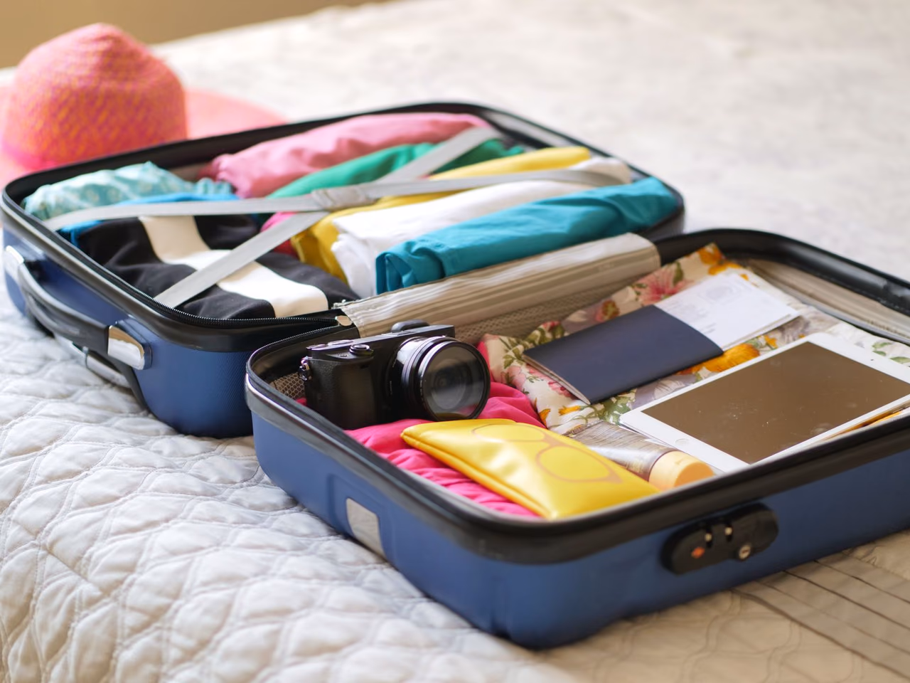 An open suitcase packed with folded clothes, a camera and a passport
